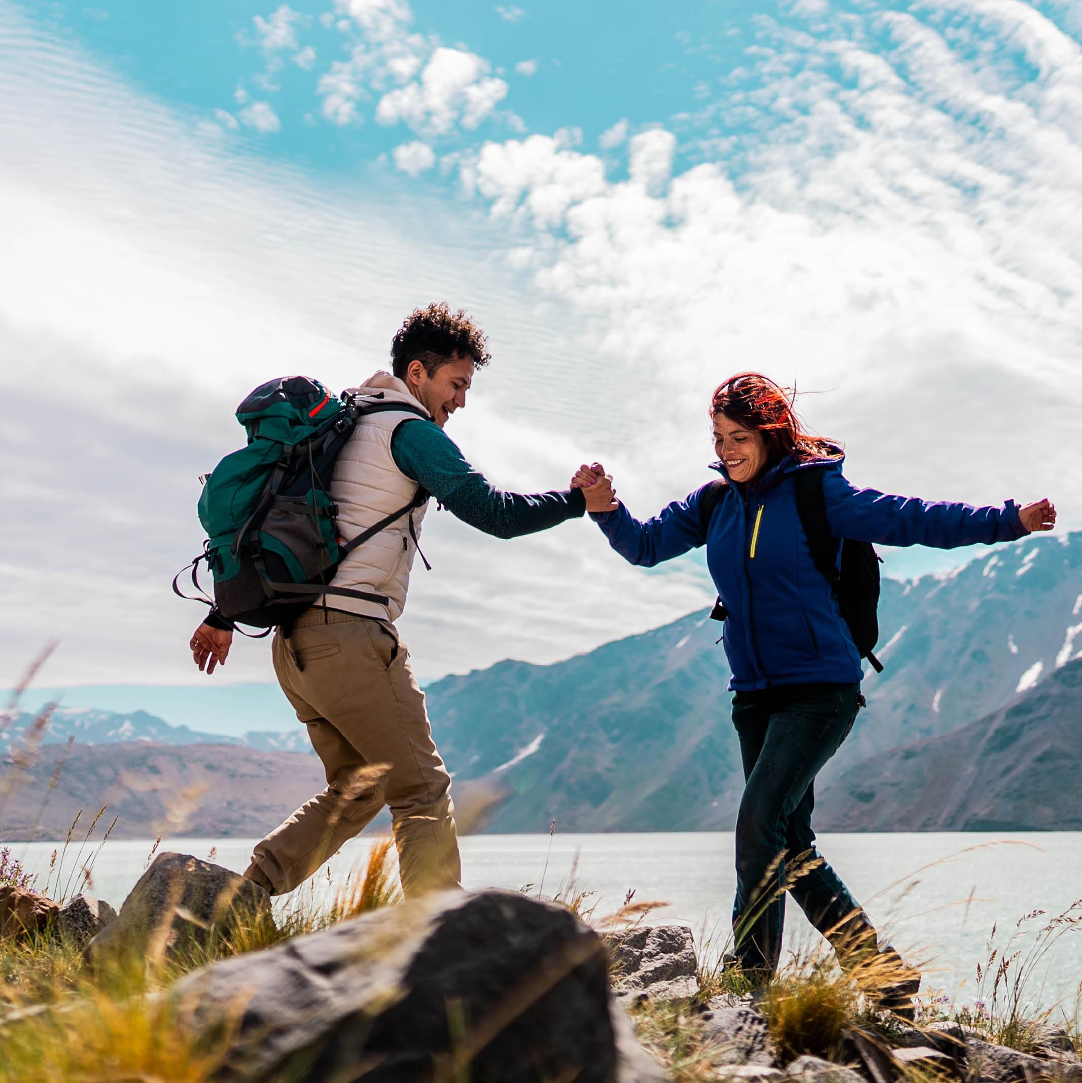 Two travelers helping each other up a mountain trail